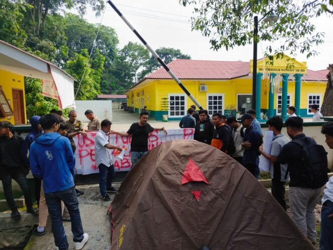 
Usai berorasi, puluhan massa dari aliansi mahasiswa mendirikan tenda di depan Kantor Dinas PMD Kabupaten Langkat, Rabu (26/6/2024) siang.